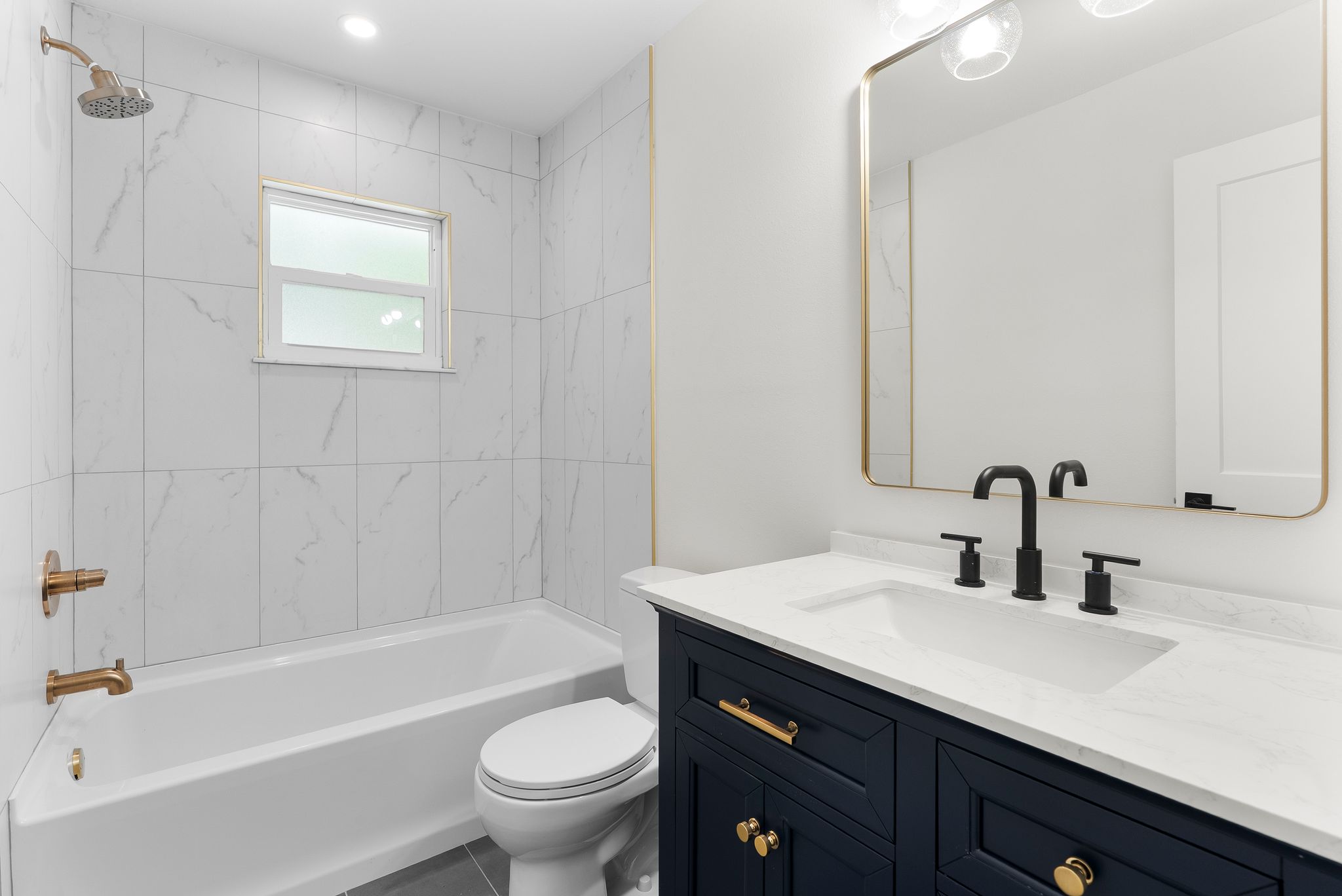 Second bathroom after - navy vanity, marble tile, gold hardware